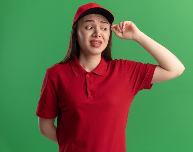 Anxious pretty delivery woman in uniform looks at side on green
