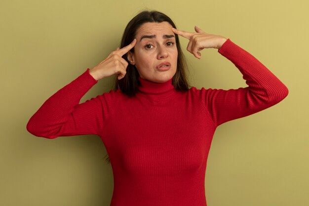 Anxious pretty woman puts fingers on temples isolated on olive green wall