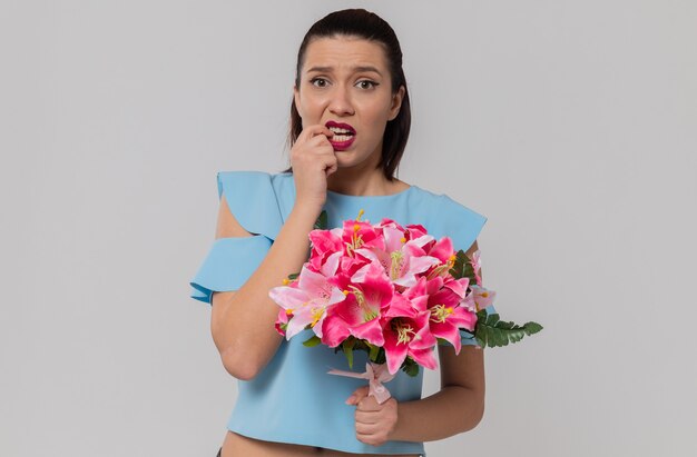 Тревожная симпатичная молодая женщина держит букет цветов и кусает ноготь