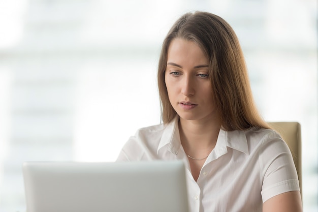 Anxious serious businesswoman working on laptop computer, looking at screen