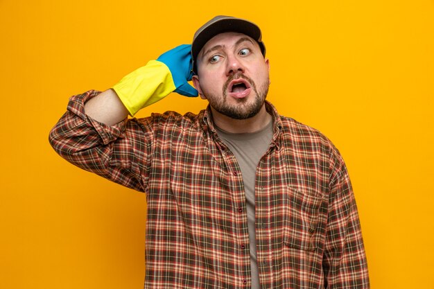 Anxious slavic cleaner man with rubber gloves putting hand on his head and looking at side