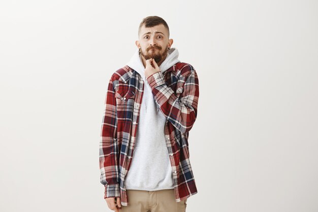 Anxious and troubled hipster guy touching beard and stooping scared