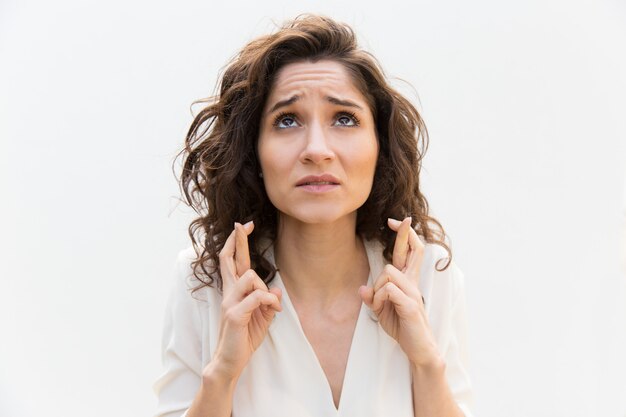 Anxious woman keeping fingers crossed and praying