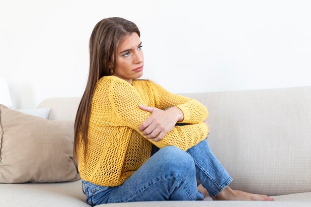 Anxious worried woman sitting on couch at home Frustrated confused female feels unhappy problems in personal life quarrel break up with boyfriend and unexpected pregnancy concept