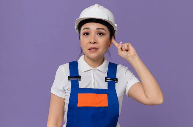 Anxious young asian builder girl with white safety helmet closing her ear with finger