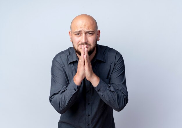 Anxious young bald call center man putting hands in pray gesture isolated on white  with copy space