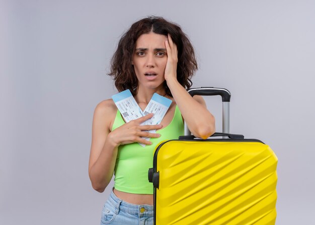 복사 공간이 격리 된 흰 벽에 비행기 티켓과 가방을 들고 불안 젊은 아름 다운 여행자 여자
