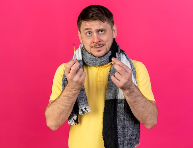 Anxious young blonde ill slavic man wearing scarf holds syringe and ampoule on pink