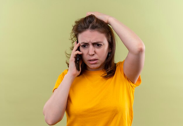 Тревожная молодая случайная женщина разговаривает по телефону с рукой за голову на изолированном зеленом пространстве с копией пространства
