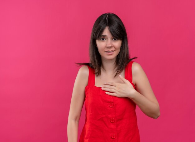 Anxious young caucasian girl holding hand on chest and looking at camera on isolated pink background with copy space