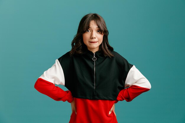 anxious young caucasian woman looking at camera biting lip while keeping hands on waist isolated on blue background