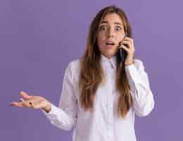 Free photo anxious young pretty caucasian girl keeps hand open and talks on phone on purple