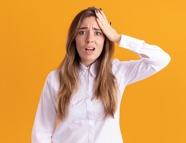 Anxious young pretty caucasian girl puts hand on forehead and looks at camera on orange 