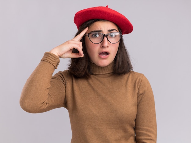Free photo anxious young pretty caucasian girl with beret hat and in optical glasses puts finger on temple on white
