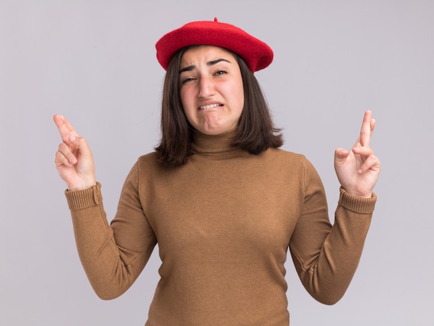 La giovane ragazza abbastanza caucasica ansiosa con il cappello del berretto sta con le dita incrociate