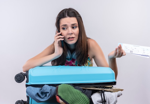 Free photo anxious young traveler woman talking on phone holding tickets on isolated white wall