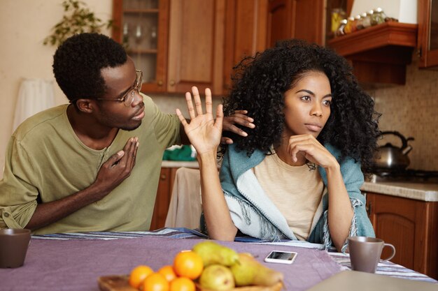 Apologetic African American male holding hand on his chest trying to convince mad woman in his fidelity. Black female ignoring her unfaithful husband's excuses. Love and relationships problems