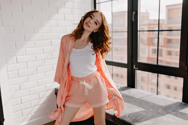 Appealing caucasian girl in pajama standing in confident pose. Stunning white lady with curly hair posing in her flat.