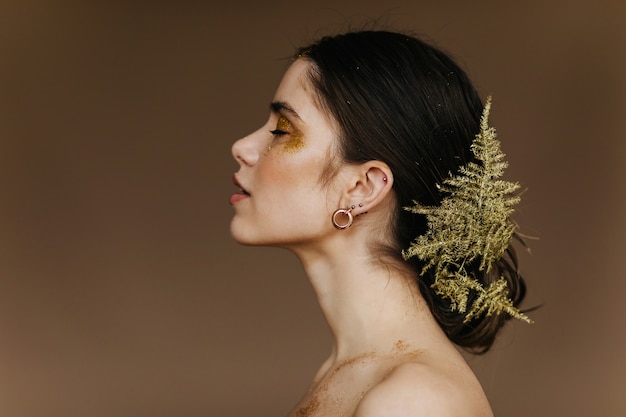 Appealing caucasian girl with plant in hair posing . Close-up portrait of cute european woman with golden earrings.