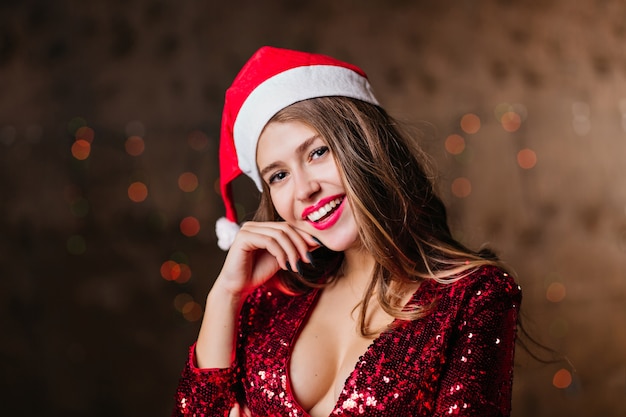 Attraente donna dai capelli lunghi in cappello di babbo natale che gode della festa