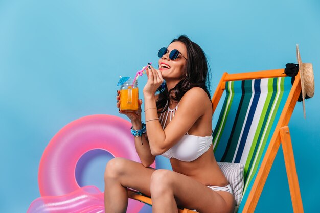 Appealing tanned woman sitting on deck chair and drinking cocktail