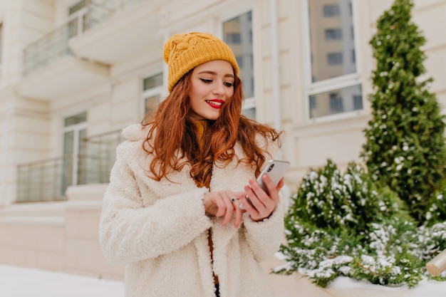 Attraente donna con messaggio di sms acconciatura lungo. ritratto di inverno della ragazza felice dello zenzero.