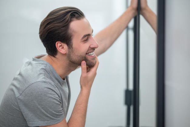 Free photo appearance. a young man in grey tshirt looking at his reflection in the mirror