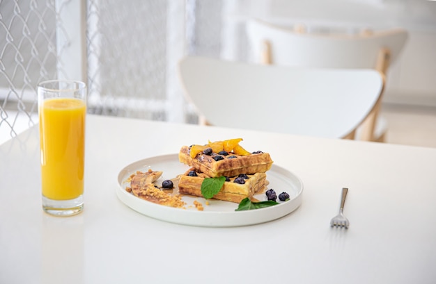 Appetitosi waffle belgi con frutti di bosco e frutta e un bicchiere di succo sul tavolo, il concetto di una deliziosa colazione.