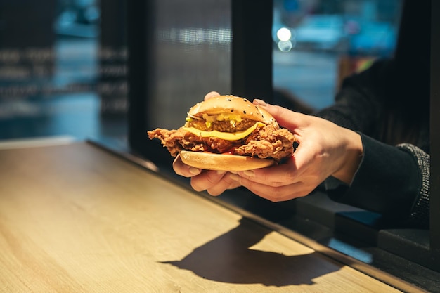 Foto gratuita un appetitoso hamburger di pollo in mani femminili in un fast food