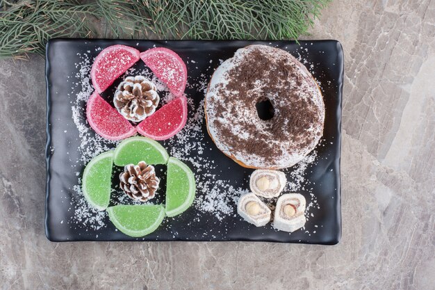 Appetizing dessert platter next to cypress leaves on marble. 