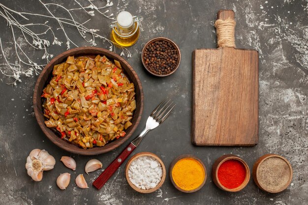 appetizing dish green beans in the plate next to the fork wooden cutting board garlic bottle of oil and bowls of spices on the dark table