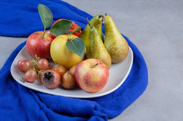 大理石の背景の青いテーブルクロスに食欲をそそるフルーツの品揃えの盛り合わせ。
