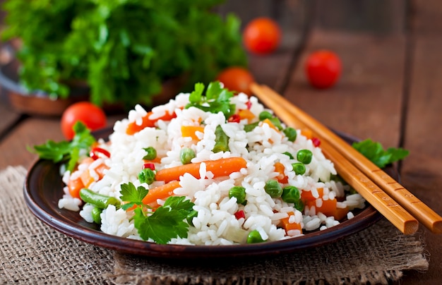 Аппетитный здоровый рис с овощами в белой плите на деревянном столе.