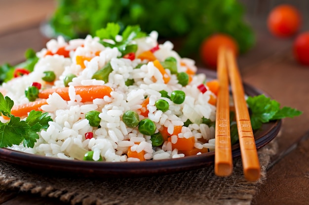 Appetizing healthy rice with vegetables in white plate on a wooden table.