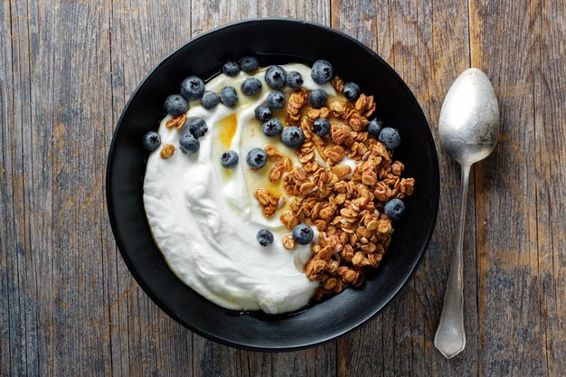 Appetizing homemade muesli with berries and yogurt served in bowl on wooden background.