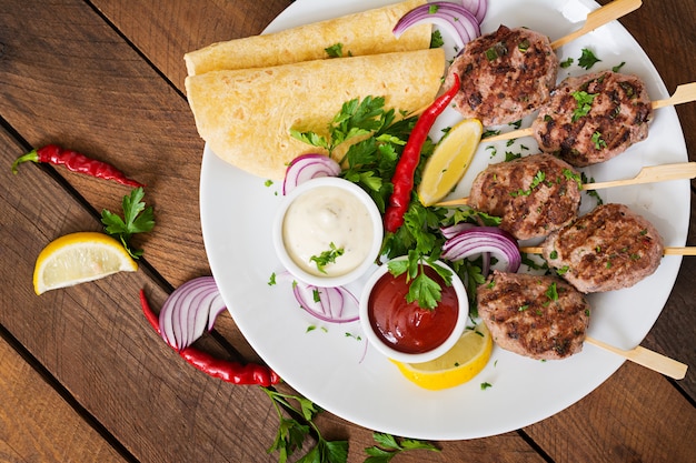 Appetizing kofta kebab (meatballs) with sauce and tortillas tacos on a white plate.
