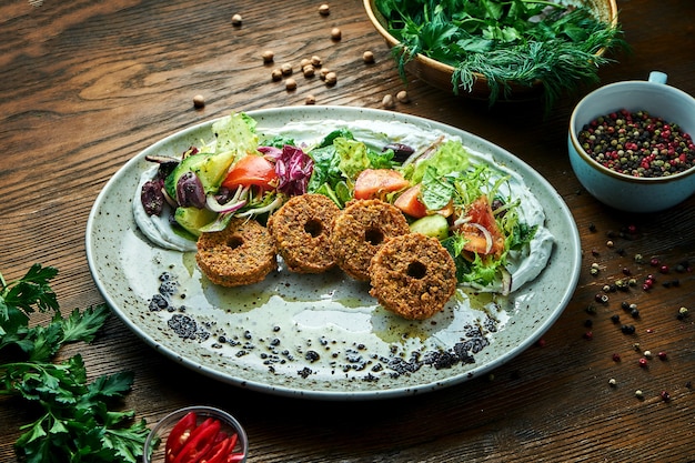 Аппетитный салат в стиле восточной кухни. салат из свежих овощей с фалафелем и оливковым маслом подается в синей тарелке на деревянном столе. еда в ресторане