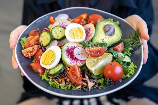 Аппетитный салат со свежими овощами и яйцами в тарелке в женских руках