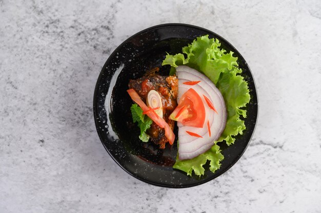 Appetizing spicy canned sardine salad in spicy sauce in black ceramic bowl