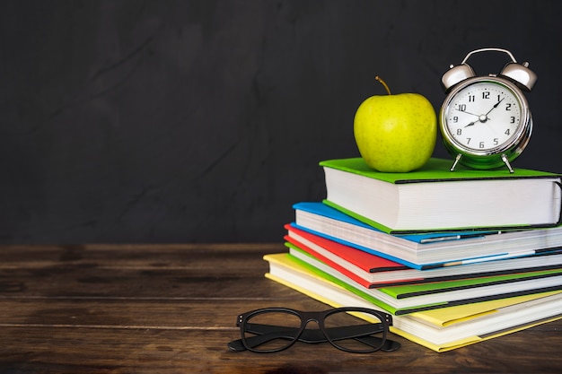 Apple and alarm clock on books with glasses on table