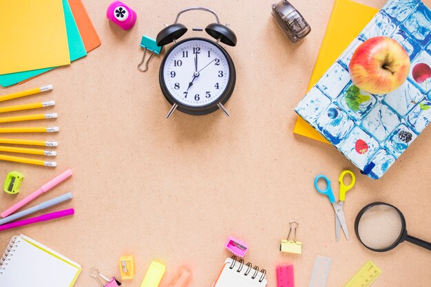 Apple and alarm clock near stationery