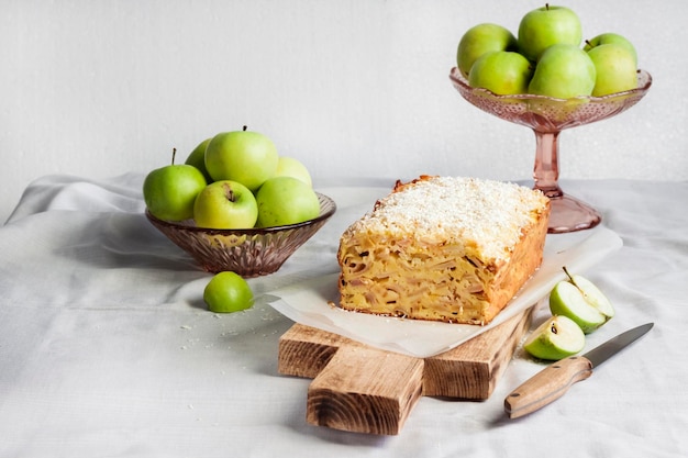 Яблочно-кокосовый пирог на деревянной разделочной доске и яблоки в вазе Premium Фотографии