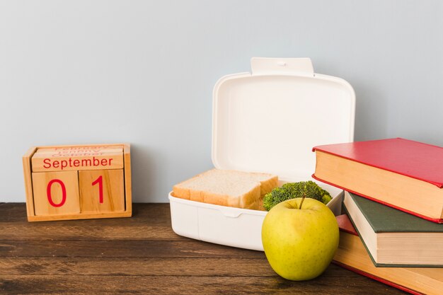 Apple and lunchbox between calendar and books