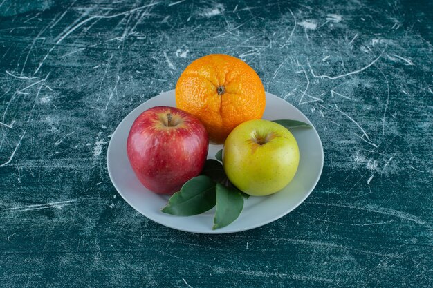 Apple, orange and leaves on a plate , on the marble table. 