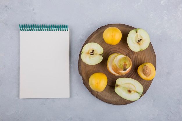 Apple, pear and peaches on a piece of wood, with a notebook aside