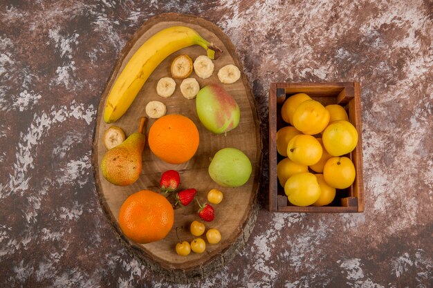 Apple, pear and peaches in a wooden box with berries aside, top view