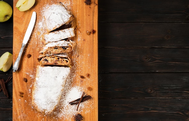 Apple pie with caramelized apples, nuts, cinnamon and raisins, cut into slices, is located on a wooden cutting board. Dish of European cuisine. Mock up on wooden table with copy space