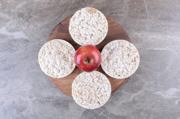 Apple and puffed rice cakes on the wooden tray, on the marble background.