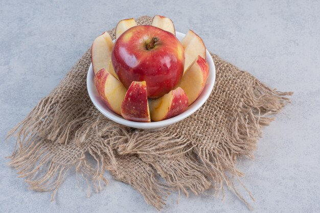 Apple slices and whole apple in white bowl. 