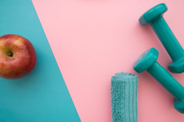Apple, towel and dumbbells on blue and pink background